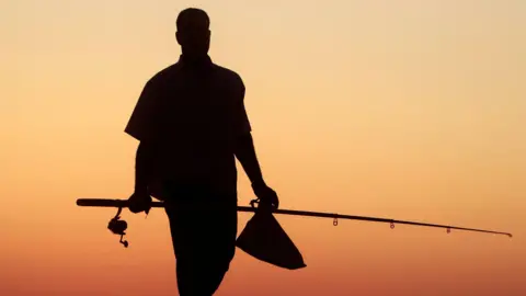 Reuters A silhouette of a person carrying a fishing rod and bag in front of a dramatic orange sunset.