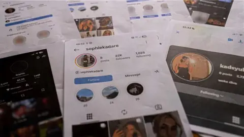 Seven A4 print outs of screenshots of the Sophie Kadare fake accouts laid out on a table. The main image in the middle shows the instagram account, which has 22k followers and eight posts, filled with Sasha's images. 