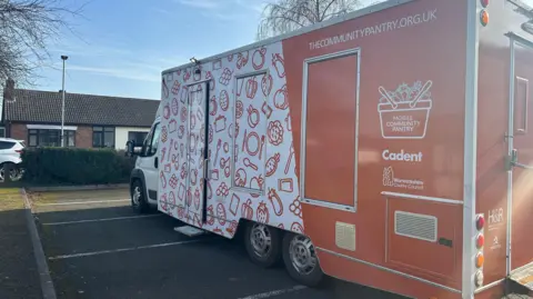 An orange van with the community pantry at the back.