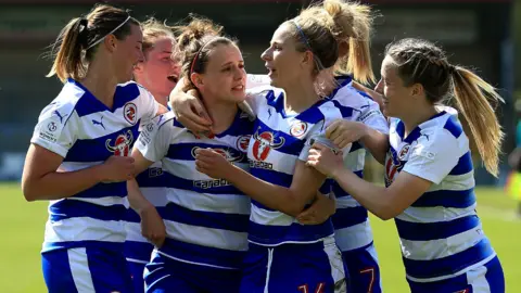 A Reading football player celebrates after scoring her team's second goal of the game. There are six female football players in the picture all hugging.