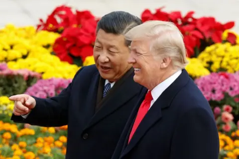 Getty Images Xi Jinping and Trump point fingers while standing in front of flowers in Beijing, 2017