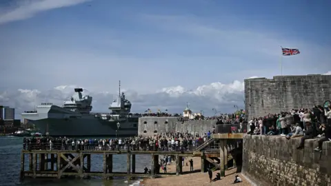 Getty Images Members of the public gather to watch British aircraft carrier HMS Prince of Wales leave from Portsmouth Naval Base on the south coast of England, on April 22, 2025, for deployment to the Indo-Pacific region.