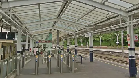 A platform at Durham station. It is covered by a large glass roof supported by metal poles with ticket barriers in the foreground.