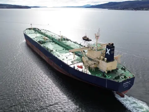 Christopher Brindle A large oil tanker sails away from the camera. The ship is black and red with green painted decks