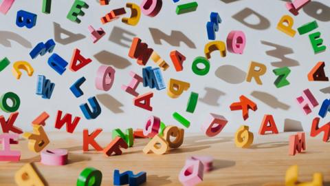 Conceptual image of colourful falling letters, casting shadows on a white wall