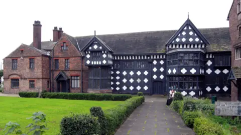 habiloid/Geograph Historic Ordsall Hall in Salford taken in 2008. A woman is sitting in the gardens near the Tudor hall. 