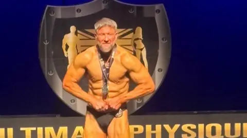 Clint Trayhern The image is split into two sections. On the left, a highly muscular individual is standing on a stage under bright lighting, performing a bodybuilding pose. On the right, a close‑up scene shows an individual drinking from a clear glass containing raw eggs.