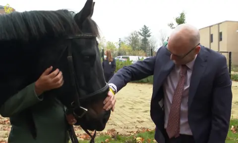 A resident at the Brainkind clinic meets Remy at a therapy session in York. The horse has dark skin and hair, with the participant wearing a suit and tie. 