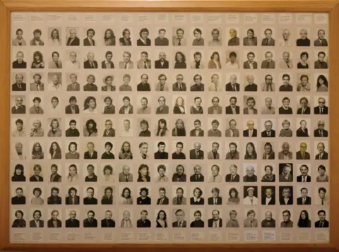Philip Sharkey Large framed display containing a grid of many small black‑and‑white portrait photographs arranged in rows and columns. Each portrait shows a single individual, with printed names or labels above or below the images.