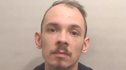 PSNI A balding brown haired man has a short brown moustache and short brown beard.