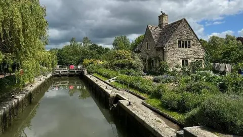 A stone cottage next to a lock and canal in the spring sunshine