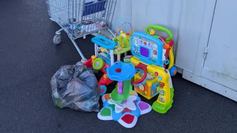 Enfys Foundation Children toys and a black bin bag left on the car park floor outside charity shop