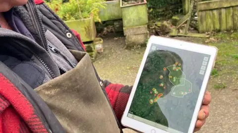 Tubuh dan tangan petani Colin Abel dapat dilihat memegang iPad dan di layar adalah rekaman GPS dari tanahnya dengan lokasi ternaknya ditandai.