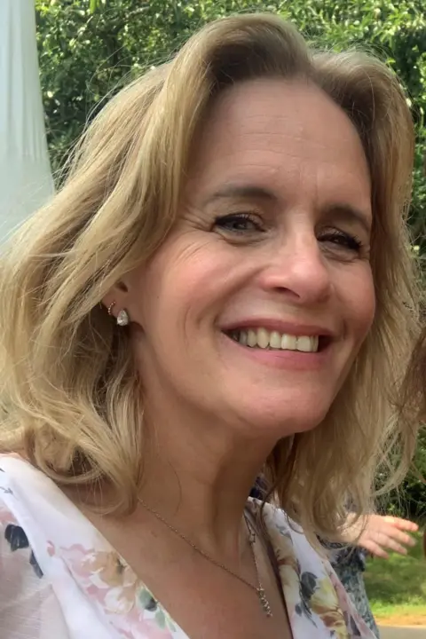 Beaulieu Convent School Tania du Bois has long blonde hair and is smiling at the camera as she stands outside with trees behind her. She is wearing a pastel-coloured floral top.