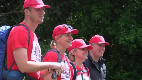 Four people stood in a line wearing matching red caps and red tshirts.