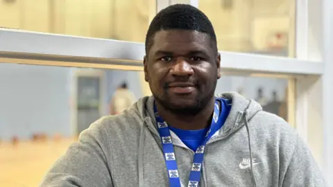 Keiren is pictured wearing a grey Nike zip hoodie and a blue lanyard