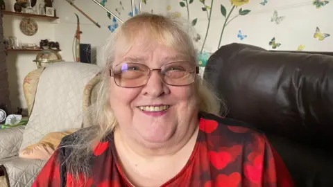 Blonde woman with glasses in a red top sat on a sofa