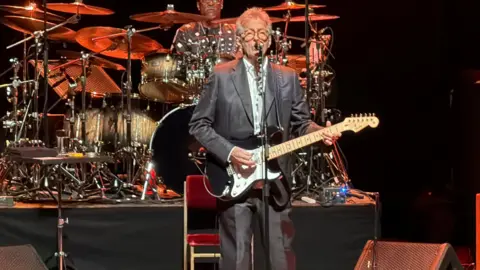 A man, Eric Clapton, stood holding a guitar while performing on a stage.