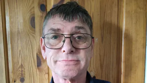 Supplied A headshot of Hughie Bruce. He is wearing glasses and standing in front of a wooden door. He is looking directly into the camera.