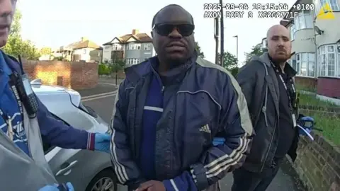 Simon Levy pictured after being arrested by police. He is wearing sunglasses and a blue sports jacket outside a building.