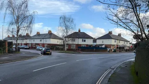 Google maps street view of St Paul's Road and the junction for Folly Lane in Cheltenham. There are cars on the road and houses on the street. 