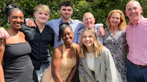 The final four teams from Race Across The World are huddled together with arms around each other and smiling. They are all smartly dressed. Pictured: Letitia, Fin, Elizabeth, Tom, Melvyn, Sioned, Caroline and Brian