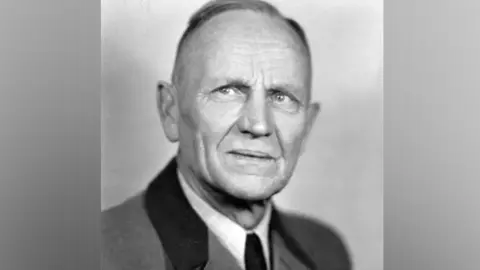 Philipp Cross Alexander Pfeifer pictured in 1940 wearing a suit, the picture is black and white and he is smiling a small smile, staring to the left of the camera