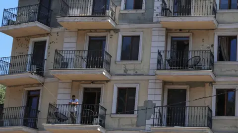 A resident stands on a balcony of an apartment building damaged by a Russian missile strike, amid Russia's attack on Ukraine, in Odesa, Ukraine July 15, 2026. 