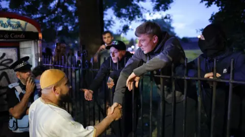 Reuters Protesters outside mosque shake hands with a worshipper, watched by a policeman