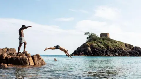 Andy Le Gresley Group of people are diving into the turquoise seas of Portelet Bay. 