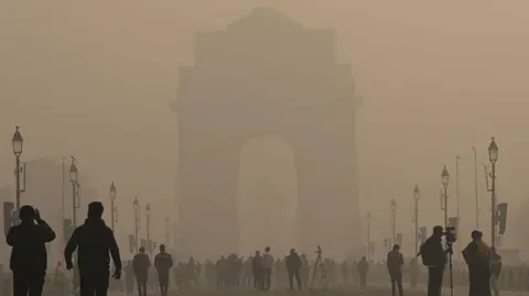Getty Images Morning smog seen in Delhi's Kartavya Path on 14 December 2025, as the view of the India Gate seems to get blurred because of haze, even as people walk around the area in the daytime