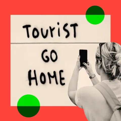 Getty Images A sign that reads "tourist go home" and a woman photographing it
