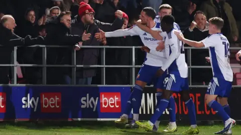 Reuters Four Swindon town players in blue and white going to shake the hands of fans standing against railings by the pitch 