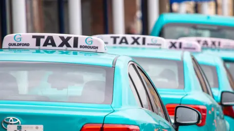 A line of taxis parked up on a street. 