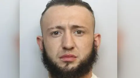 Wiltshire Police Mugshot of Michael Bowers in a white T-shirt. He has dark hair and a beard. 