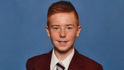 BBC School photograph of William Lindsay - a red headed teenager wearing a burgundy school blazer and tie, smiling looking into the camera