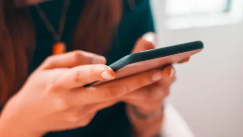 Getty Images A stock image of a woman holding a mobile phone. It is a close-up of her hands and the back of her phone.