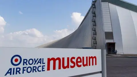 The Royal Air Force Museum in Cosford. The sign at the entrance of the museum. A towering building can be seen behind. 