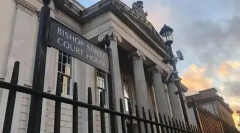 Bishop Street Courthouse in Derry. A grey building can be seen behind black railings. A sign reads: 'Bishop Street Courthouse'