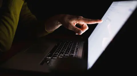 Getty Images A dark room with a person pointing at a laptop.