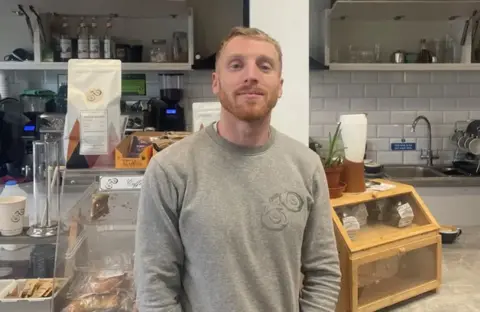 O proprietário do café, Kristian Cuffin, está em suas instalações em Holyhead.