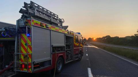A fire engine on a road, sun low in the sky.