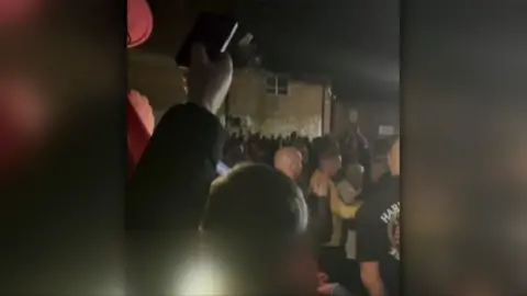 Drinks can being thrown at a large crowd in a dark car park in Bridgwater 