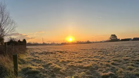 The sun is just above the horizon on a frosty field.