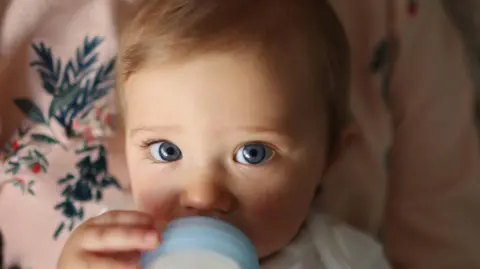 Getty Images Baby with fair hair and blue eyes drinking bottled milk