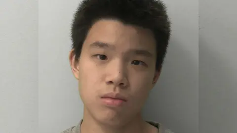 A mugshot of a boy with short black hair looking expressionless.