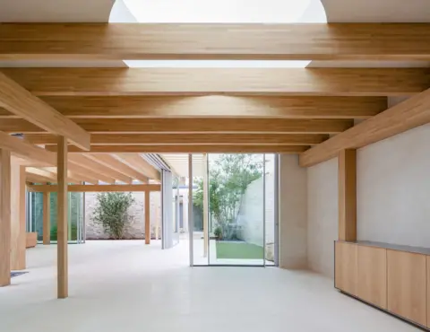 RIBA Light wooden beams overlook large glass doors on white floors with trees in the distance 