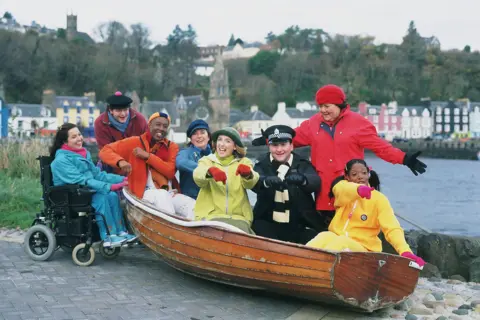 The original cast of Balamory smiling in a boat