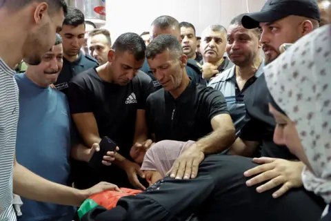 Reuters A woman lies on top of a corpse as others gather for a funeral