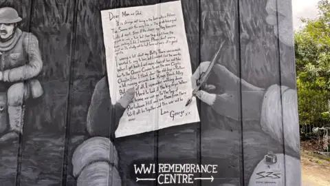 Portsmouth City Council A close up of the part of the mural that shows a handwritten letter from a soldier, George, to his parents. Underneath is a sign saying the WWI remembrance centre is to the right.